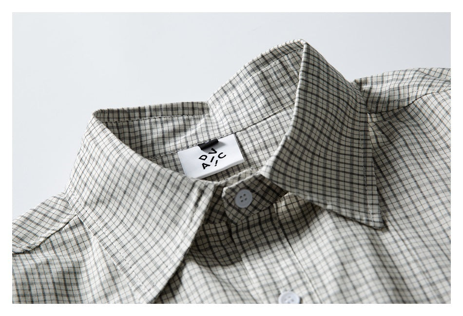 Close-up of a pointed collar and neck label on an off-white shirt with a fine black and gray check pattern.