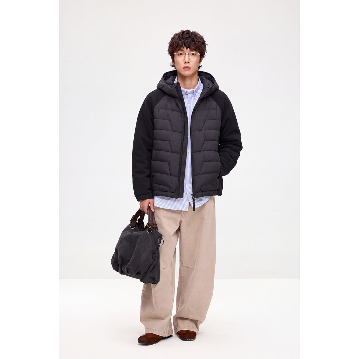 Front view of a model wearing a black hooded jacket with quilted panels, solid sleeves, and a front zipper.