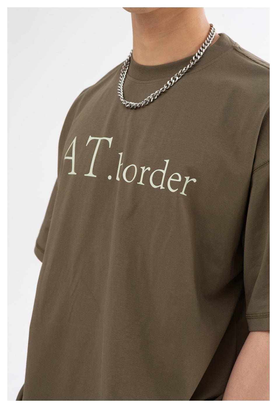 Close-up of an olive-brown T-shirt with pale lettering across the chest and a crew neckline.