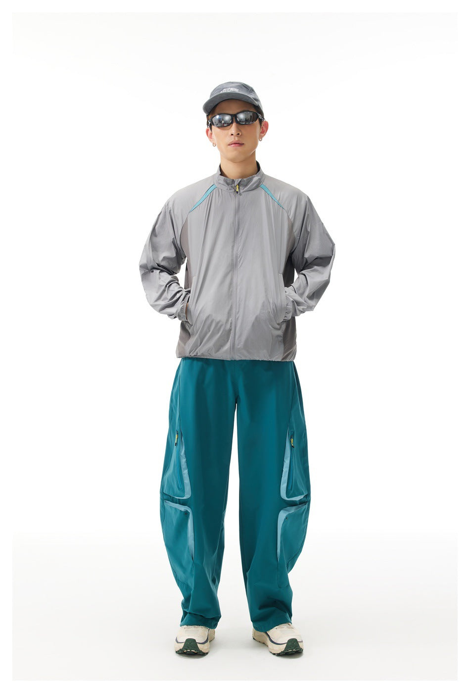 Full-length front view of a man wearing a light gray jacket with turquoise accents and teal cargo trousers.
