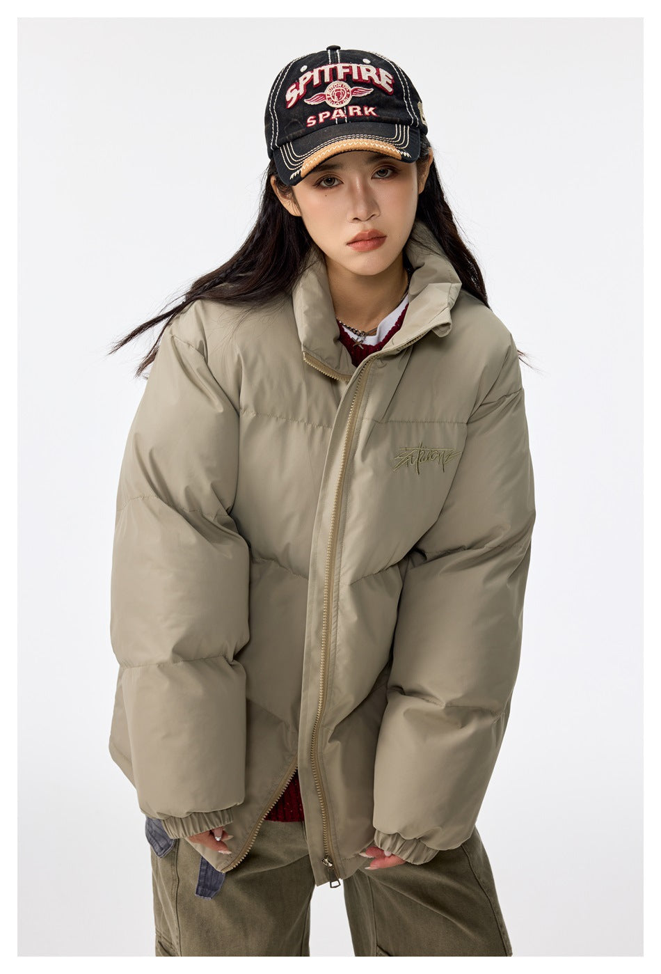 Model wearing a khaki puffer jacket with stand collar and zip, loose fit, styled with a cap and cargo pants
