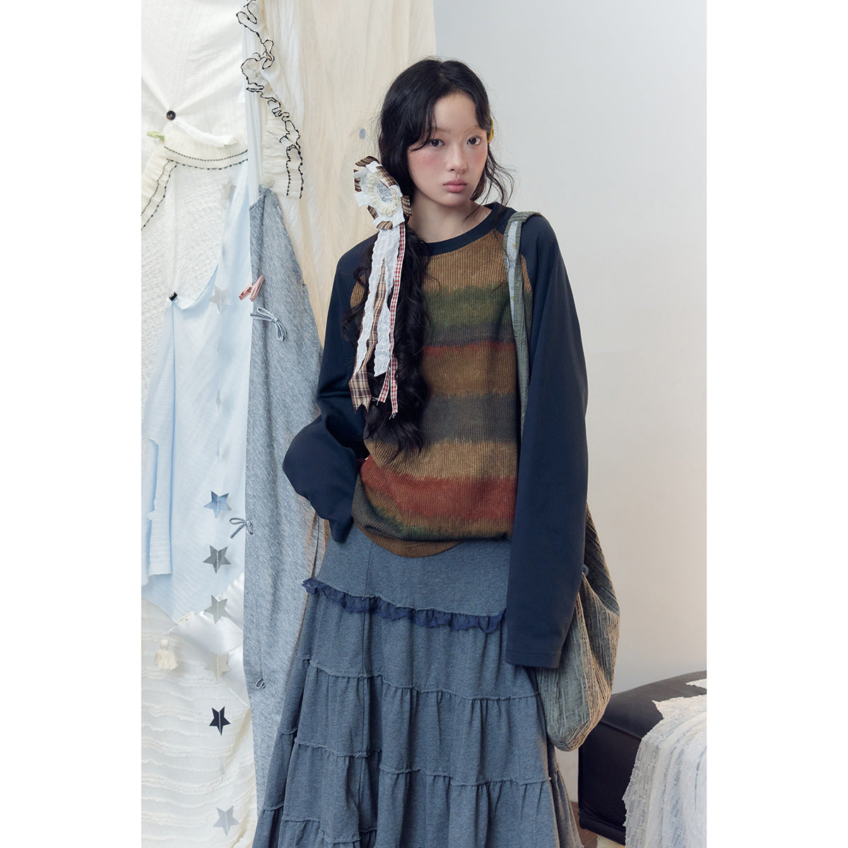 Model wearing a brown and muted multicolor striped top with navy sleeves and a long gray tiered skirt.