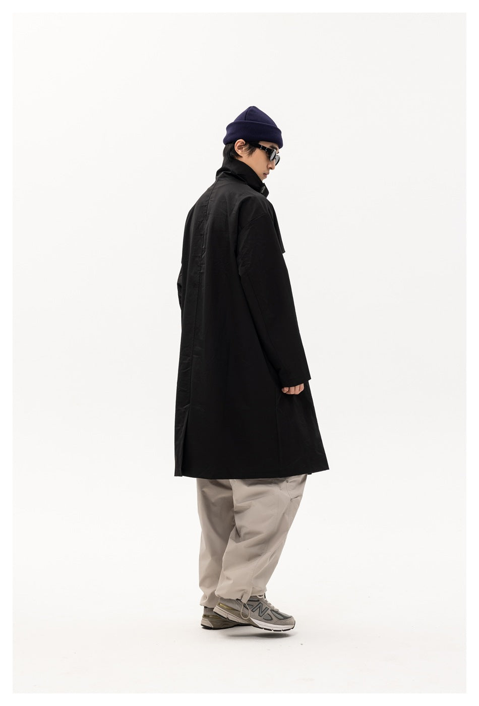 Side and rear view of a model wearing a long black coat with a straight back and a loose fit.