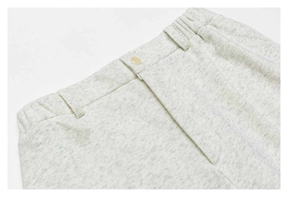Close-up of pale heathered trousers showing the waistband, button, belt loops, and fly.