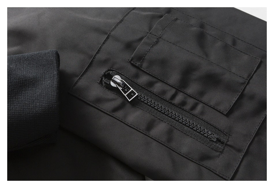 Close-up of black jacket fabric showing a chunky zipper, stitched flap pocket, and ribbed cuff.