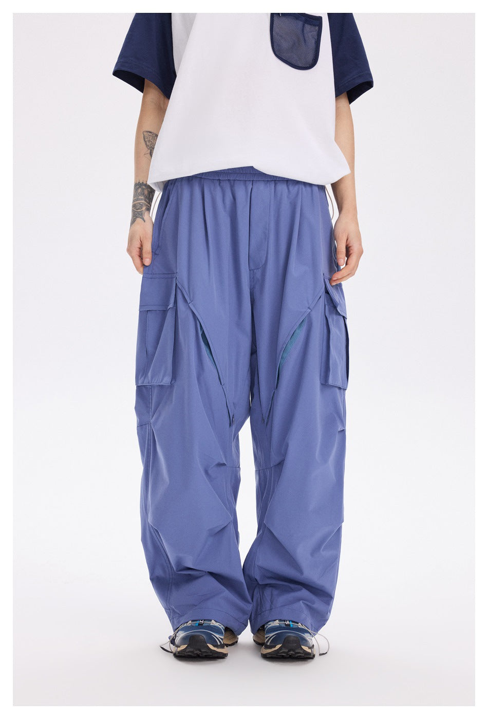 Front view of a model wearing loose periwinkle cargo pants with large flap pockets and a white and navy shirt.