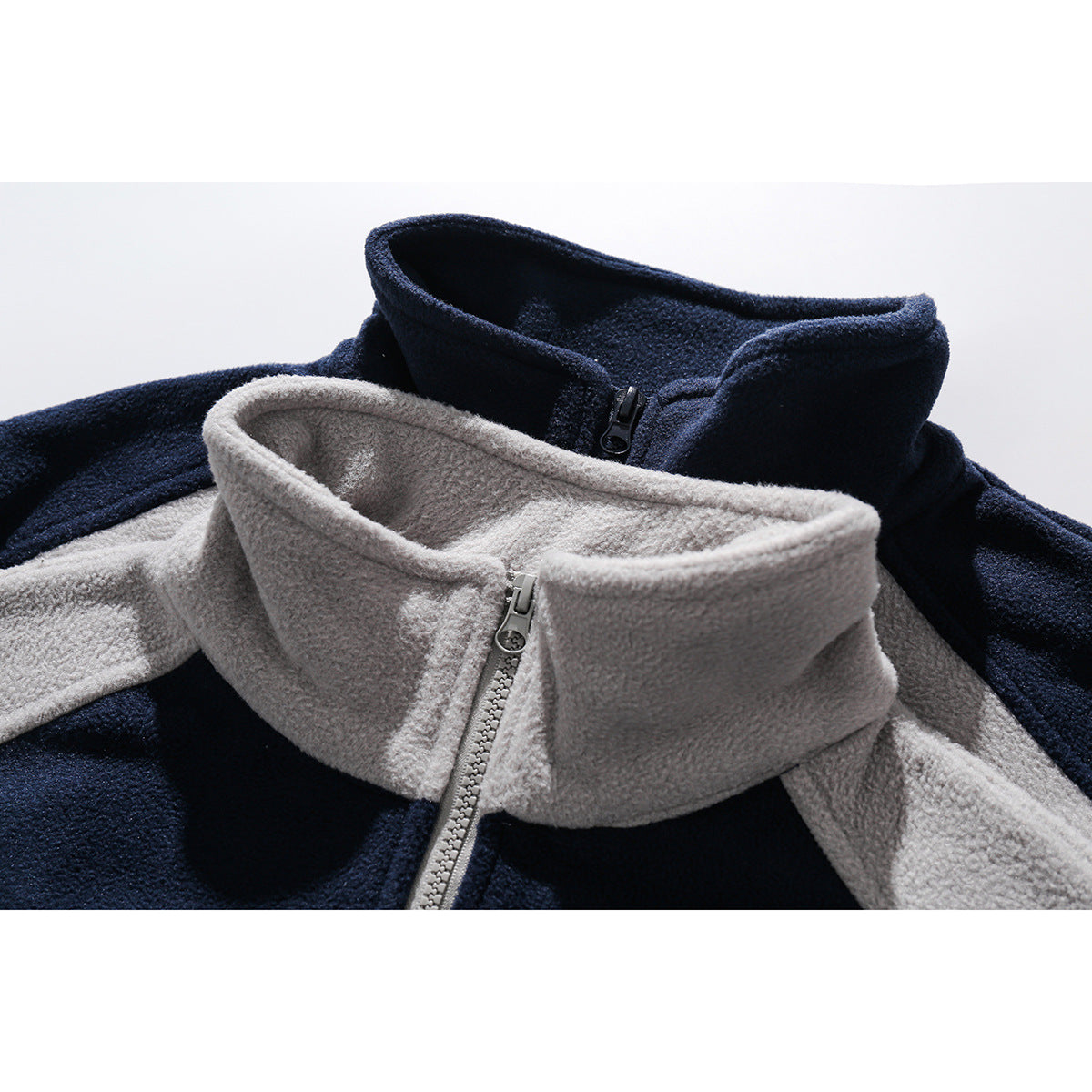 Close-up of two color-block fleece tops showing their tall zip collars in navy and light gray.