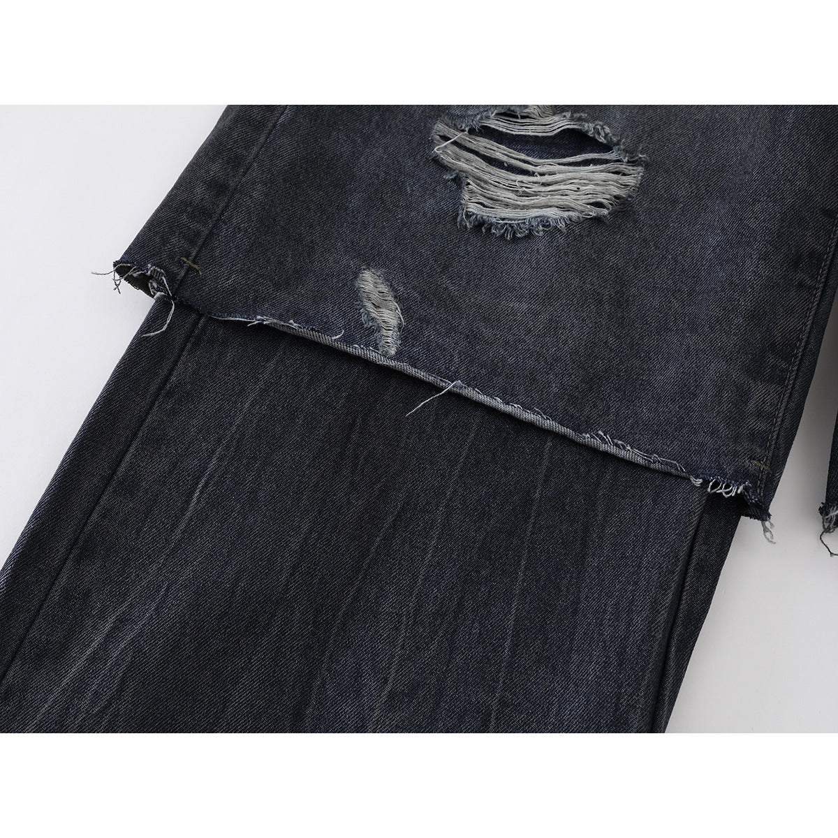 Close-up of a raw denim hem and distressed tears on dark charcoal jeans.