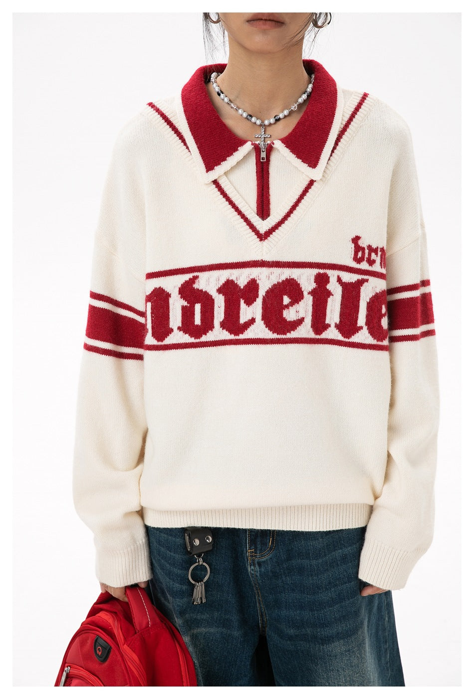 Close-up of an ivory sweater on a model, highlighting the red collar and sleeve stripes and large chest lettering.