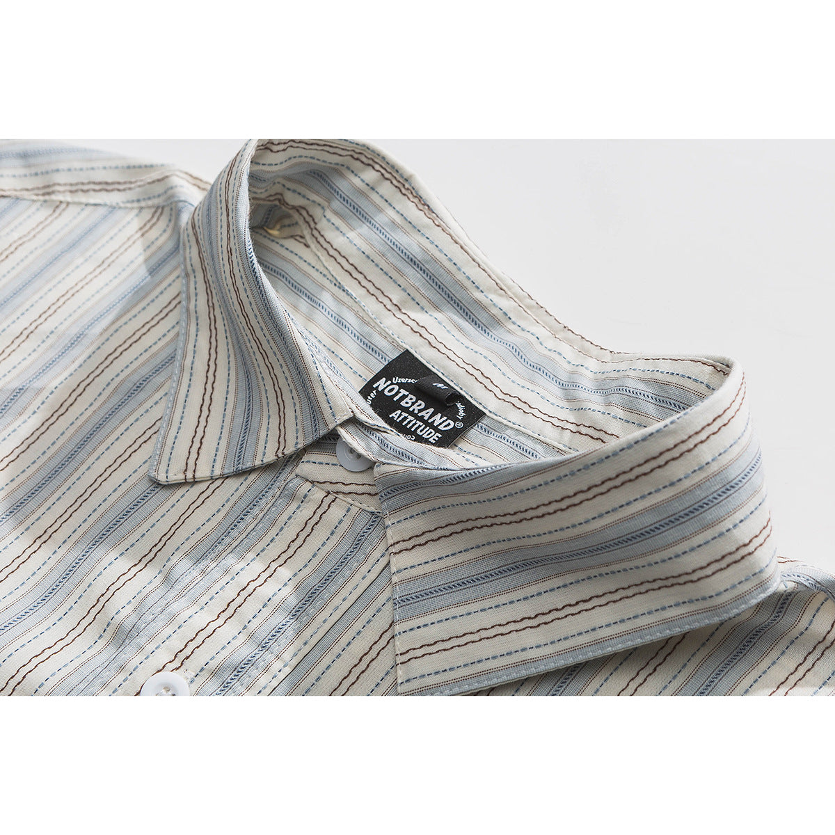 Close-up of a cream shirt collar with fine blue and brown stripes and a black sewn-in neck label.