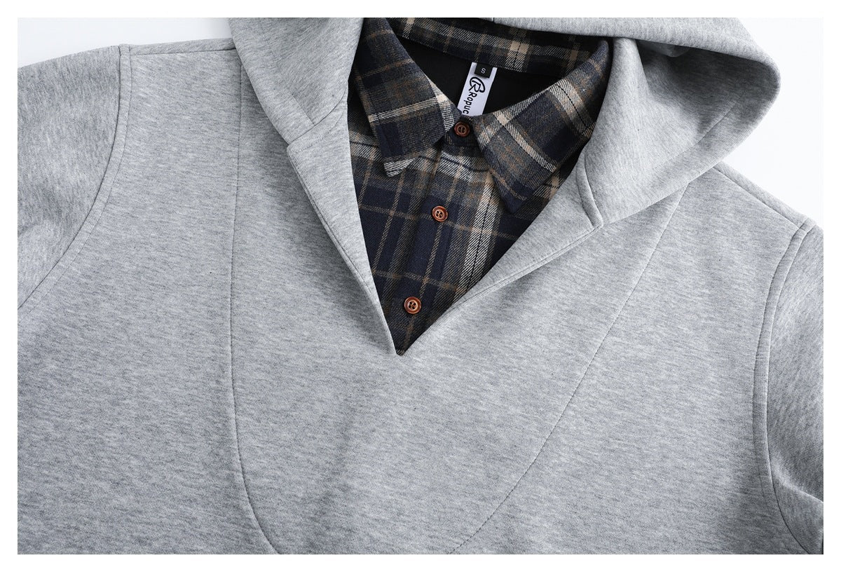 Close-up of a light gray hooded top layered over a dark plaid button-up shirt with brown buttons.