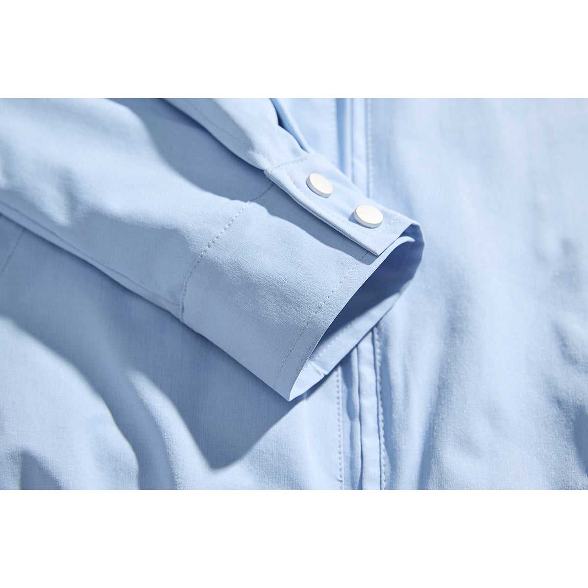 Close-up of a light blue jacket sleeve cuff with two white snaps and visible stitching.