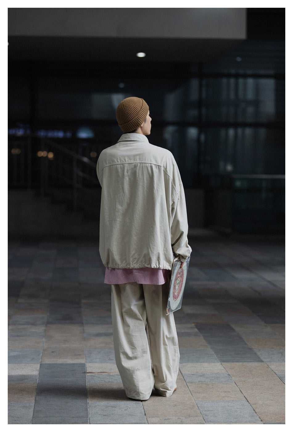 Back view of a model wearing a light gray oversized jacket with a gathered hem and wide-leg trousers.