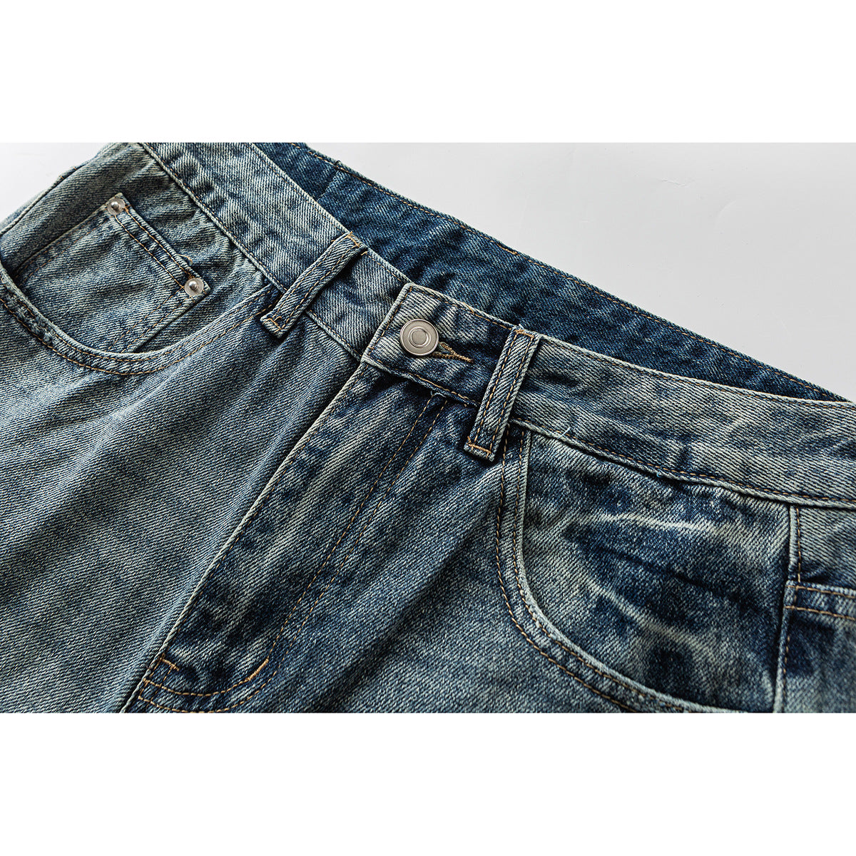 Close-up of blue acid-wash jeans showing the front waistband, button, belt loops and pockets.