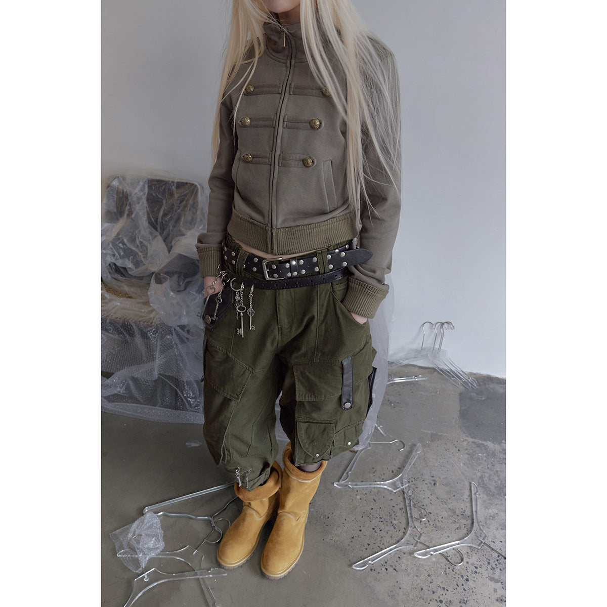 Model wearing a taupe cropped jacket and loose olive cargo pants with large pockets and strap details.