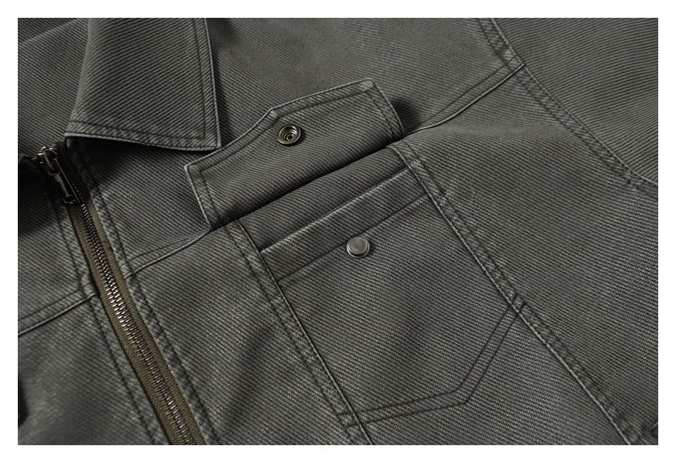 Close-up of a charcoal gray jacket chest pocket with a snap flap, beside the front zipper.
