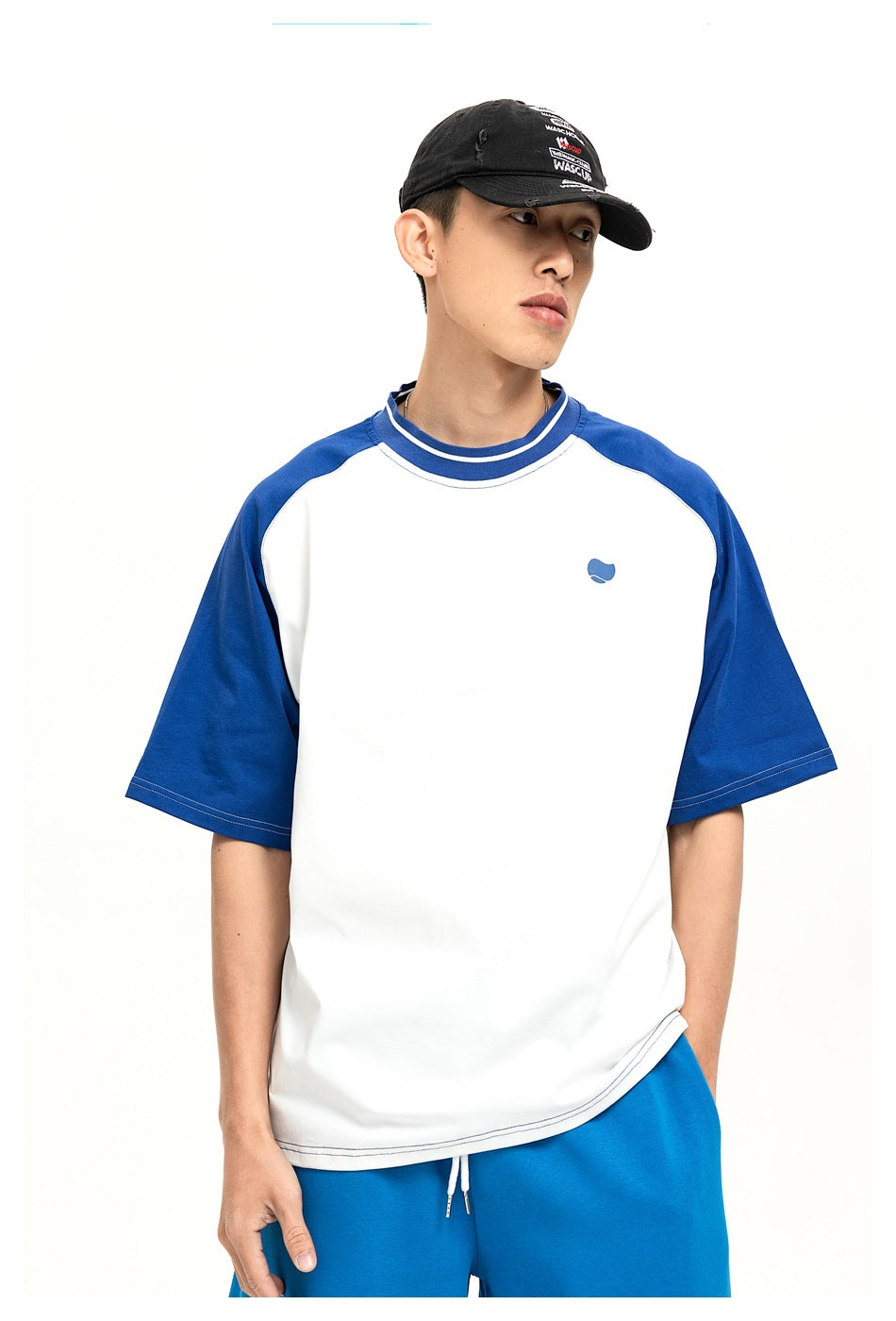 Model wearing a white T-shirt with royal blue raglan sleeves, striped collar and a small chest emblem.