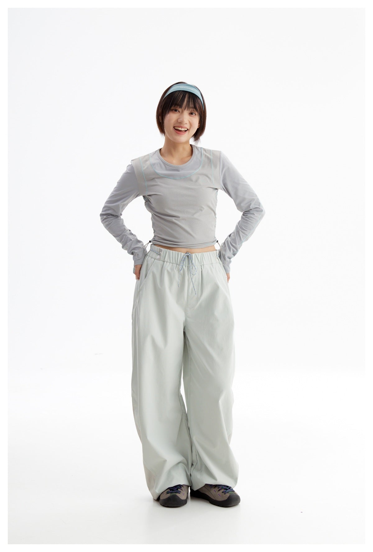 Model wearing a gray cropped long-sleeve top with aqua piping and loose pale gray drawstring pants.
