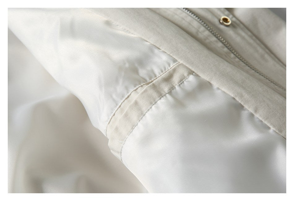 Close-up of a cream jacket sleeve seam beside the front zipper and metal eyelet.
