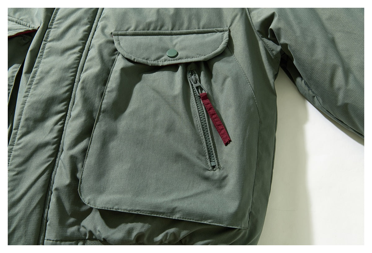 Close-up of a sage green jacket pocket with a snap flap and vertical zipper with a burgundy pull.