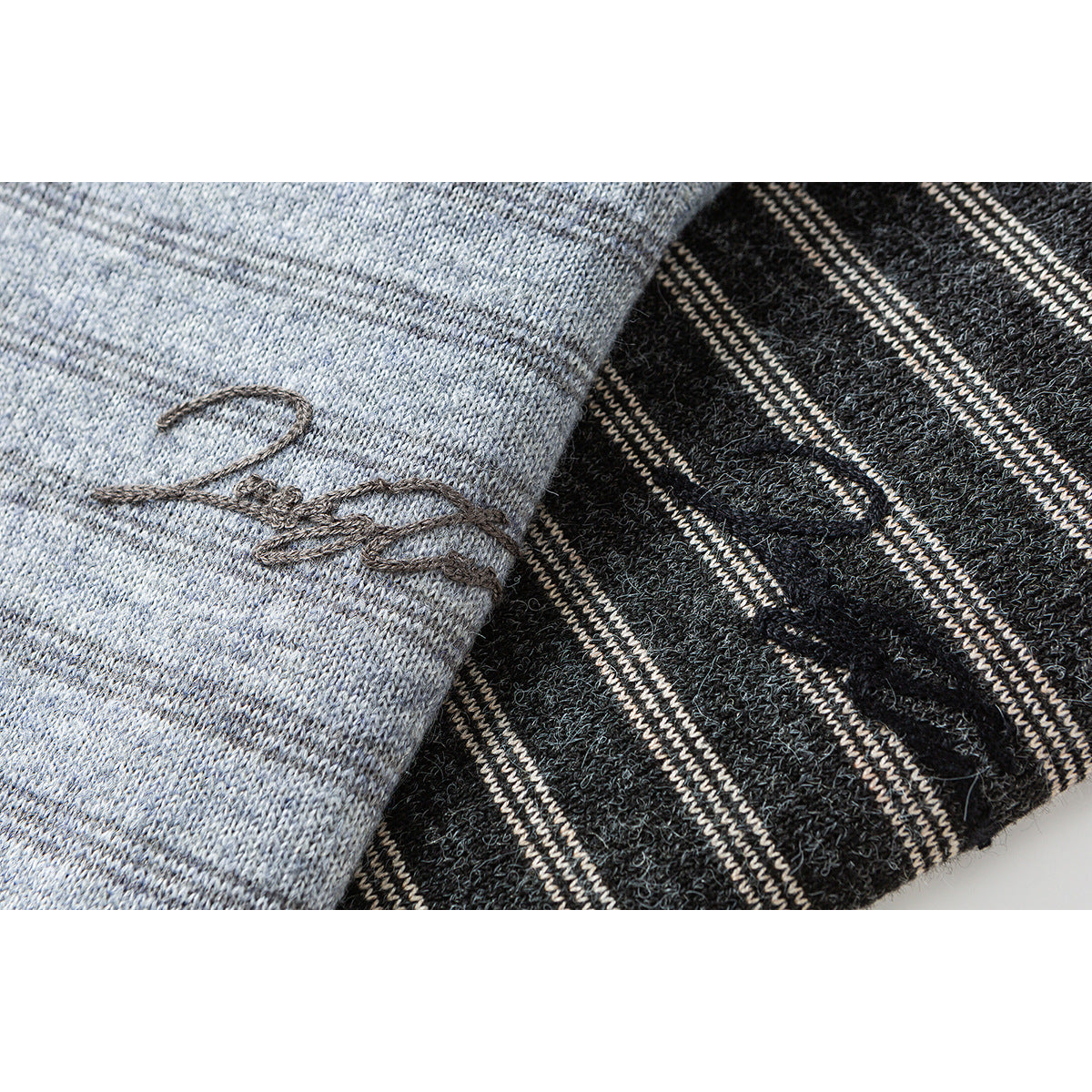 Close-up of a small dark embroidered script-like motif on light gray knit beside black-and-cream striped knit.