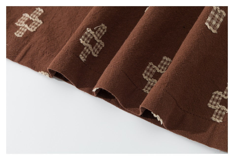 Close-up of the stitched hem and draped folds of a brown garment with cream motifs.
