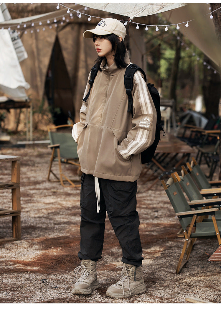 Full-length model wearing a taupe pullover jacket with cream sleeve stripes, black cargo pants, and hiking boots at a