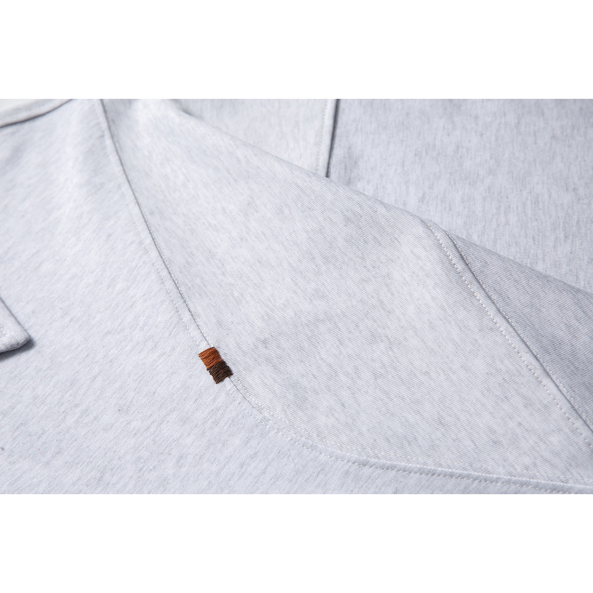 Close-up of a small brown embroidered tab and curved seam on light gray shirt fabric.