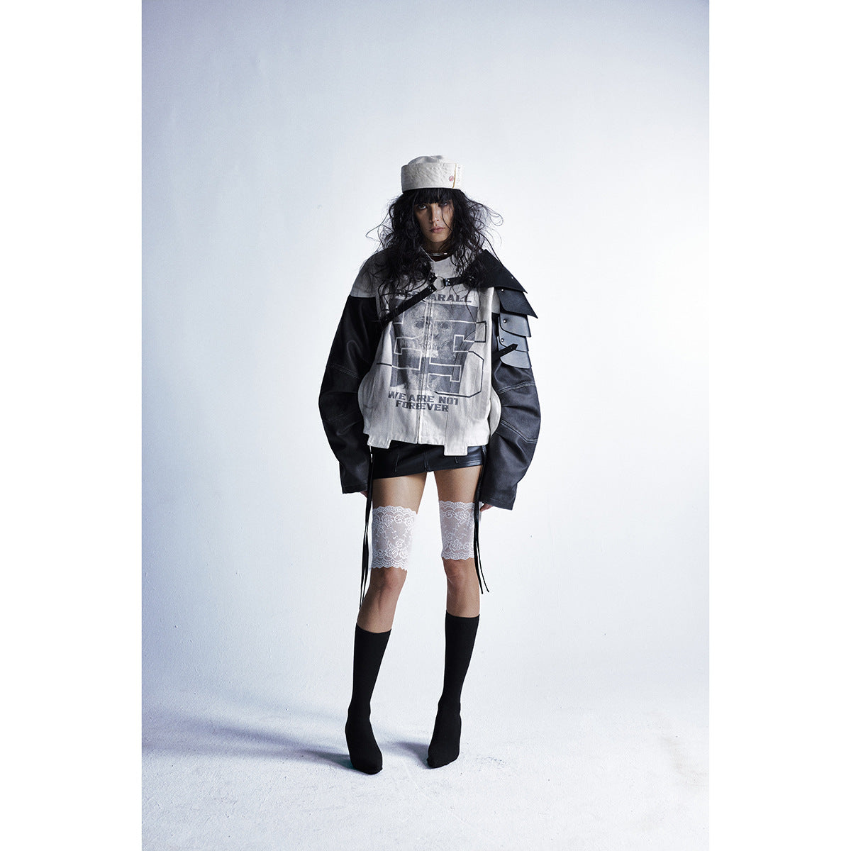 Full-length model wearing a cream-and-black graphic jacket, black mini skirt, lace thigh-highs and black socks.