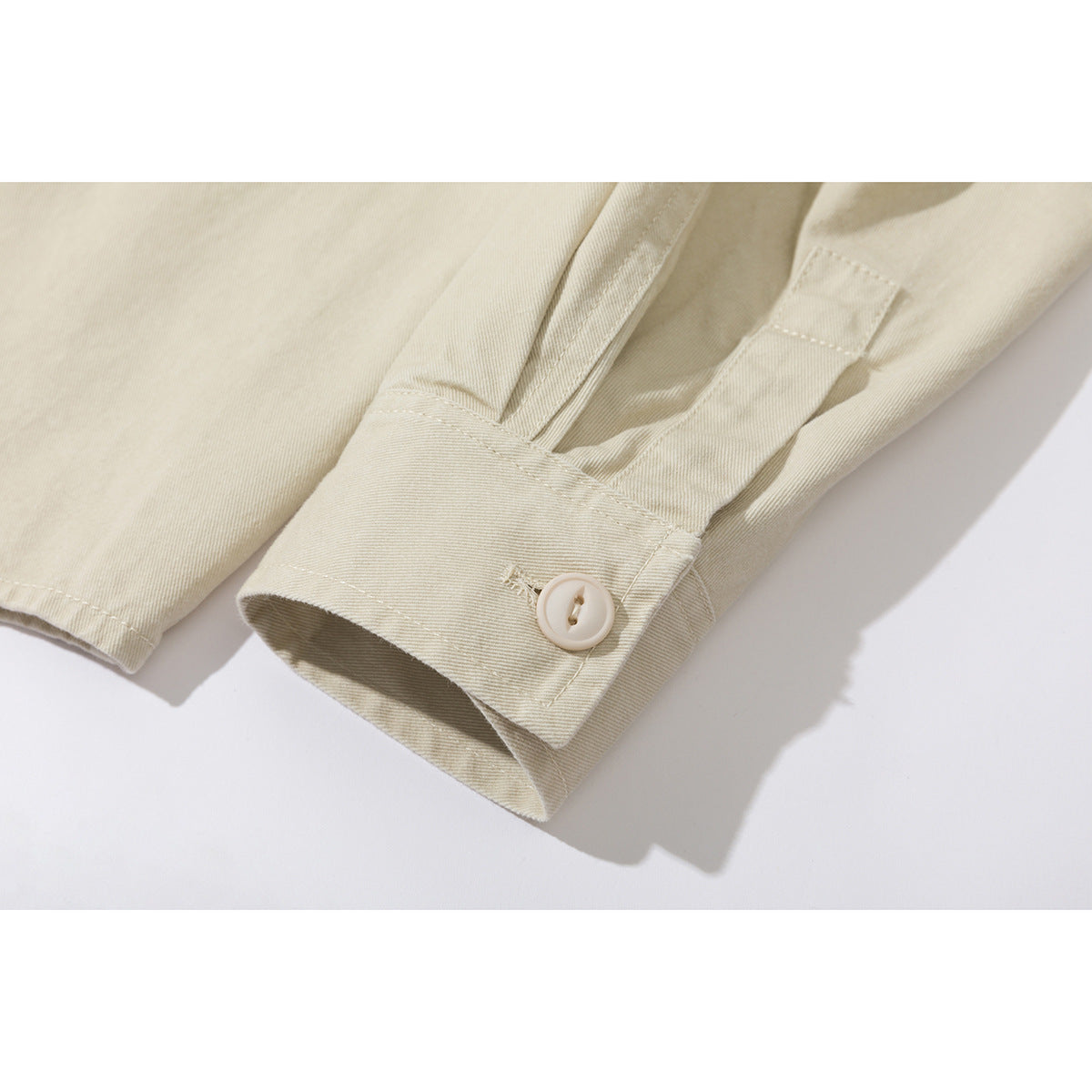 Close-up of a cream shirt sleeve cuff with a cream button and stitched details.