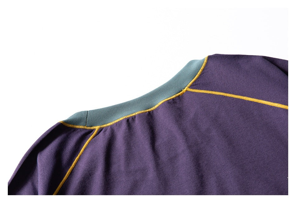 Close-up of a purple garment neckline and shoulder with a teal collar panel and mustard-yellow contrast stitching.