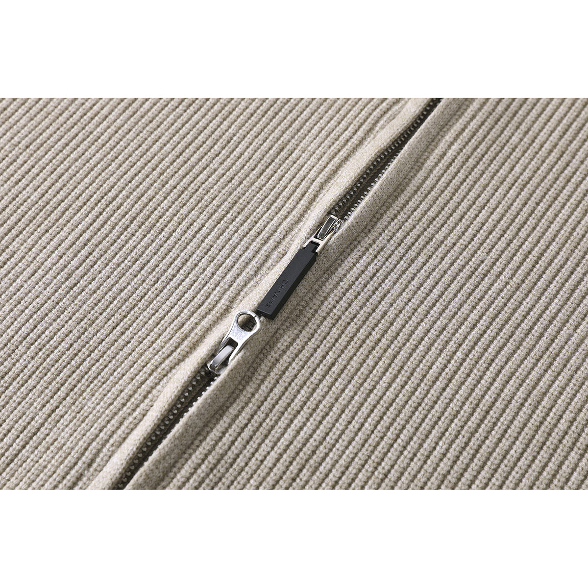 Close-up of a metal zipper and pull on cream rib-knit fabric.