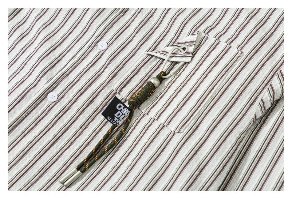 Close-up of a cream striped shirt chest pocket with a decorative cord and buttons.