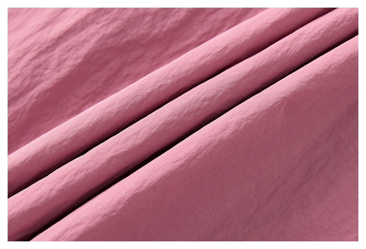 Close-up of smooth pink fabric draped in folds, showing its fine surface texture.