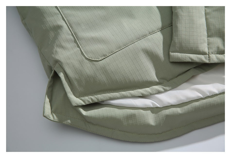 Close-up of a pale sage jacket's large patch pocket and curved hem, with white lining visible.
