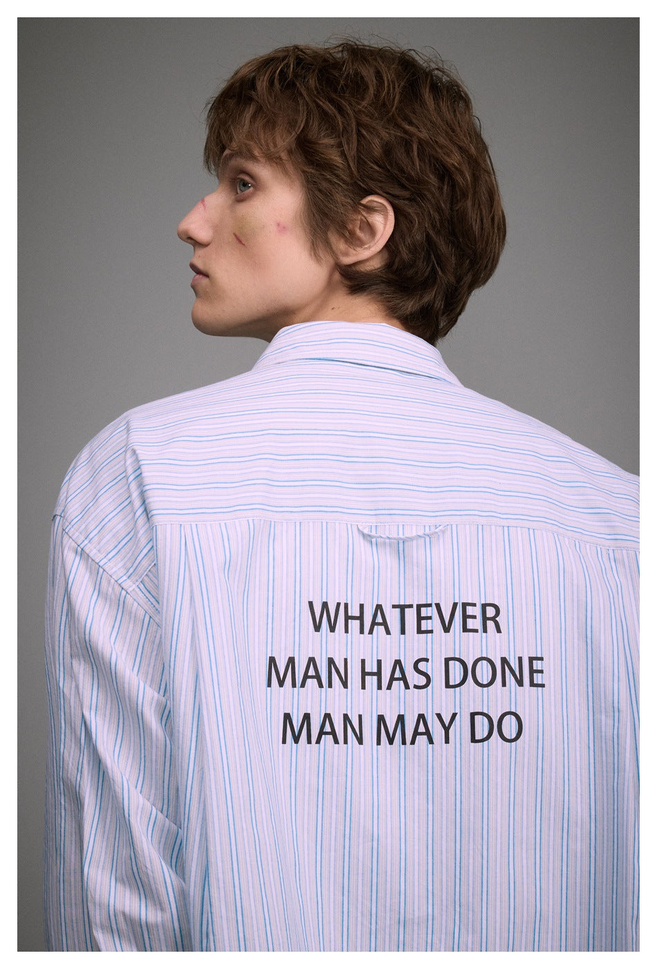 Close-up of a blue-and-white striped shirt back with the slogan “WHATEVER MAN HAS DONE MAN MAY DO.”