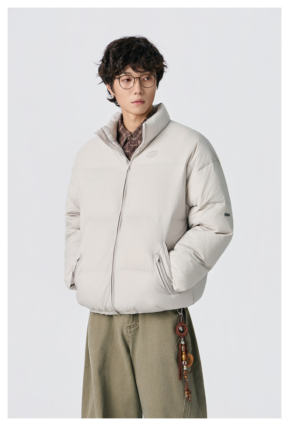 Model wearing an off-white puffer jacket with a high collar and zip pockets, styled with olive trousers.