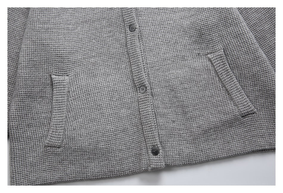 Close-up of a gray textured cardigan front with dark buttons and two slanted pockets.