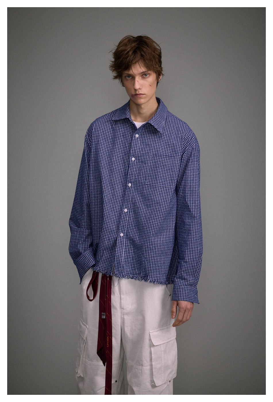 Front view of a model wearing a blue small-check button-up shirt with a frayed hem and white cargo pants.