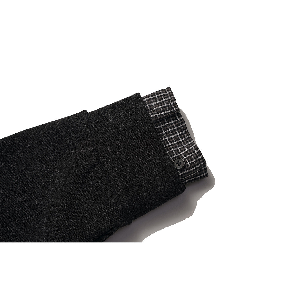 Close-up of a black cardigan cuff with a button and gray checked fabric underneath.