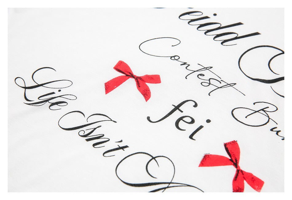Angled close-up of black cursive lettering and red bow prints on white shirt fabric.