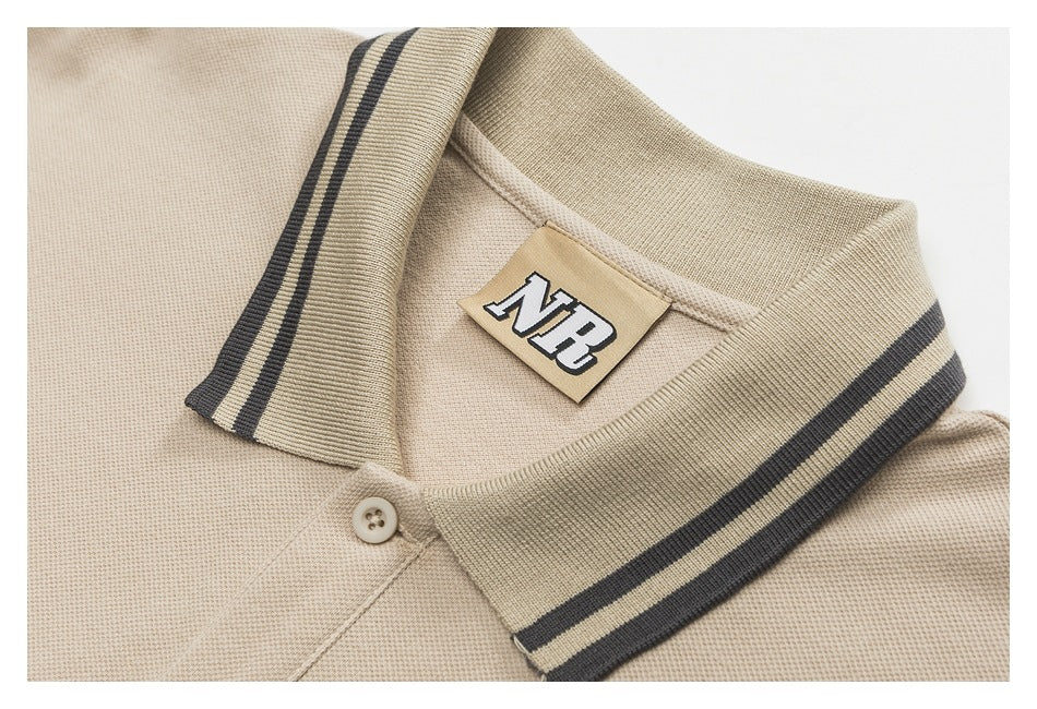 Close-up of a beige polo collar with dark striped edging, a button, and an NB neck label.