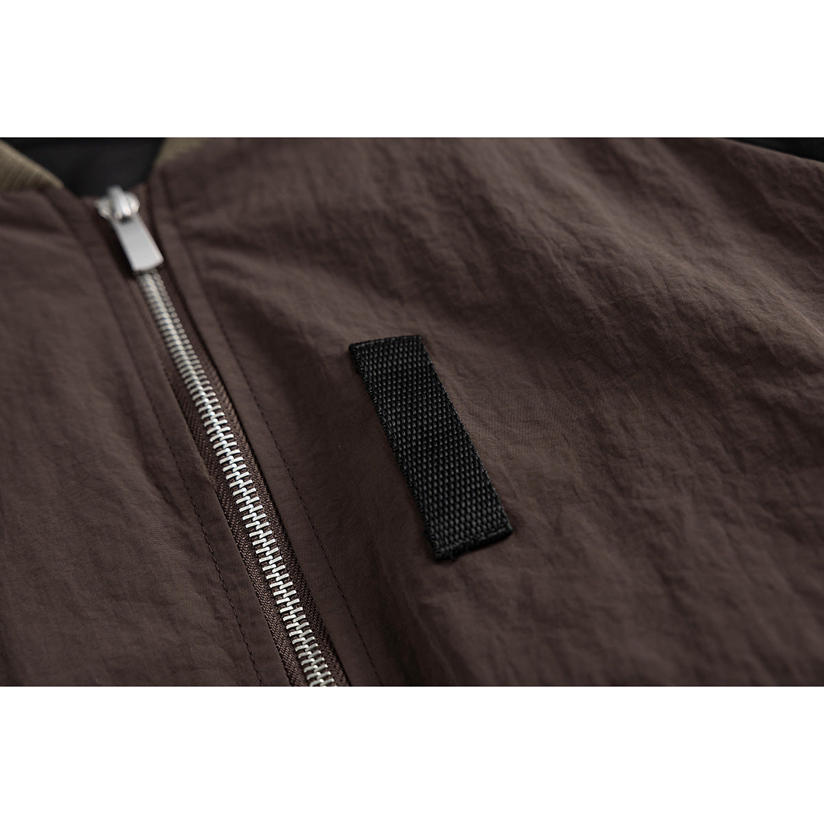 Close-up of a dark brown jacket front with a silver zipper and a narrow black fabric tab.