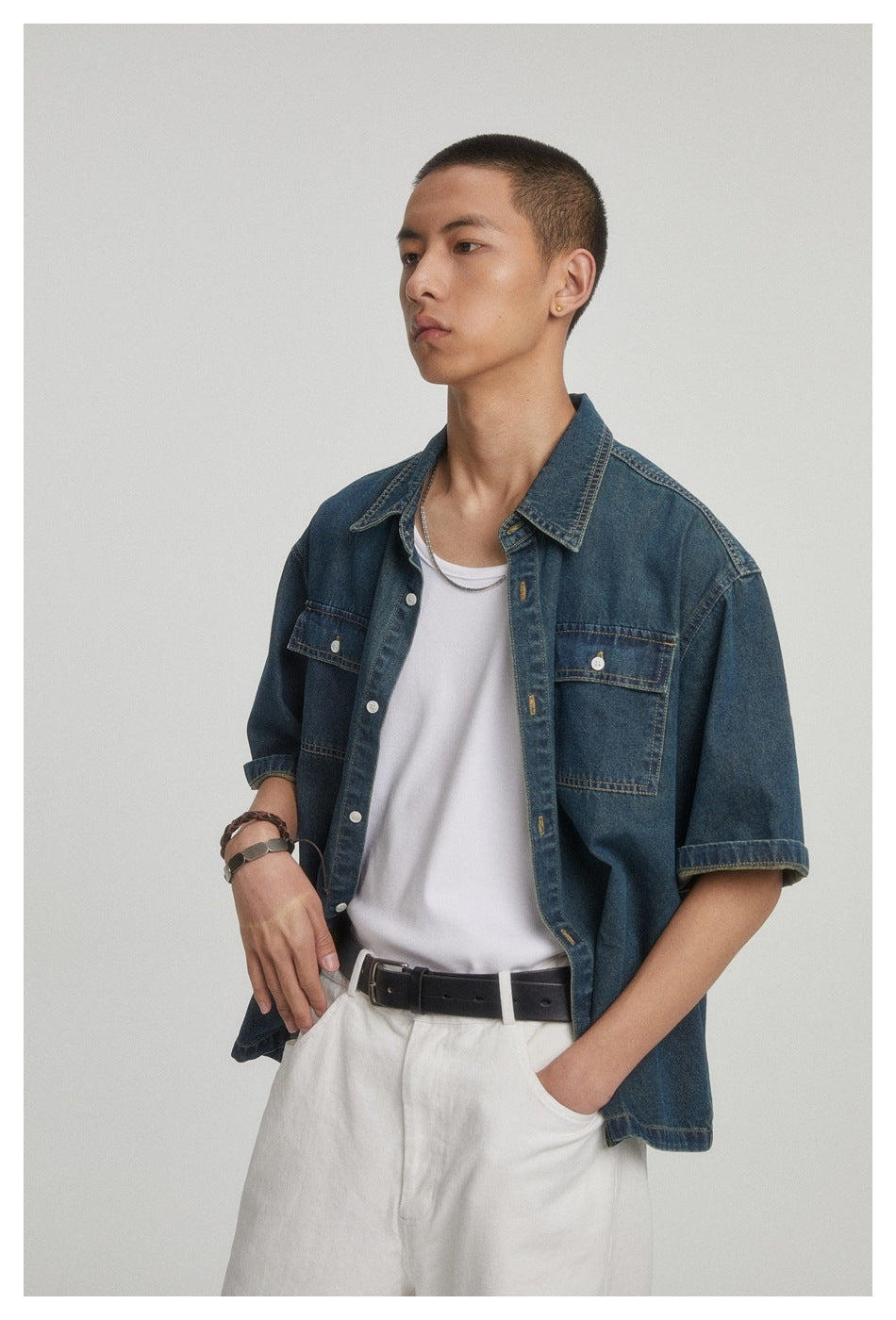 Model wearing an open dark blue denim short-sleeve shirt over a white tank top, with white pants and a black belt
