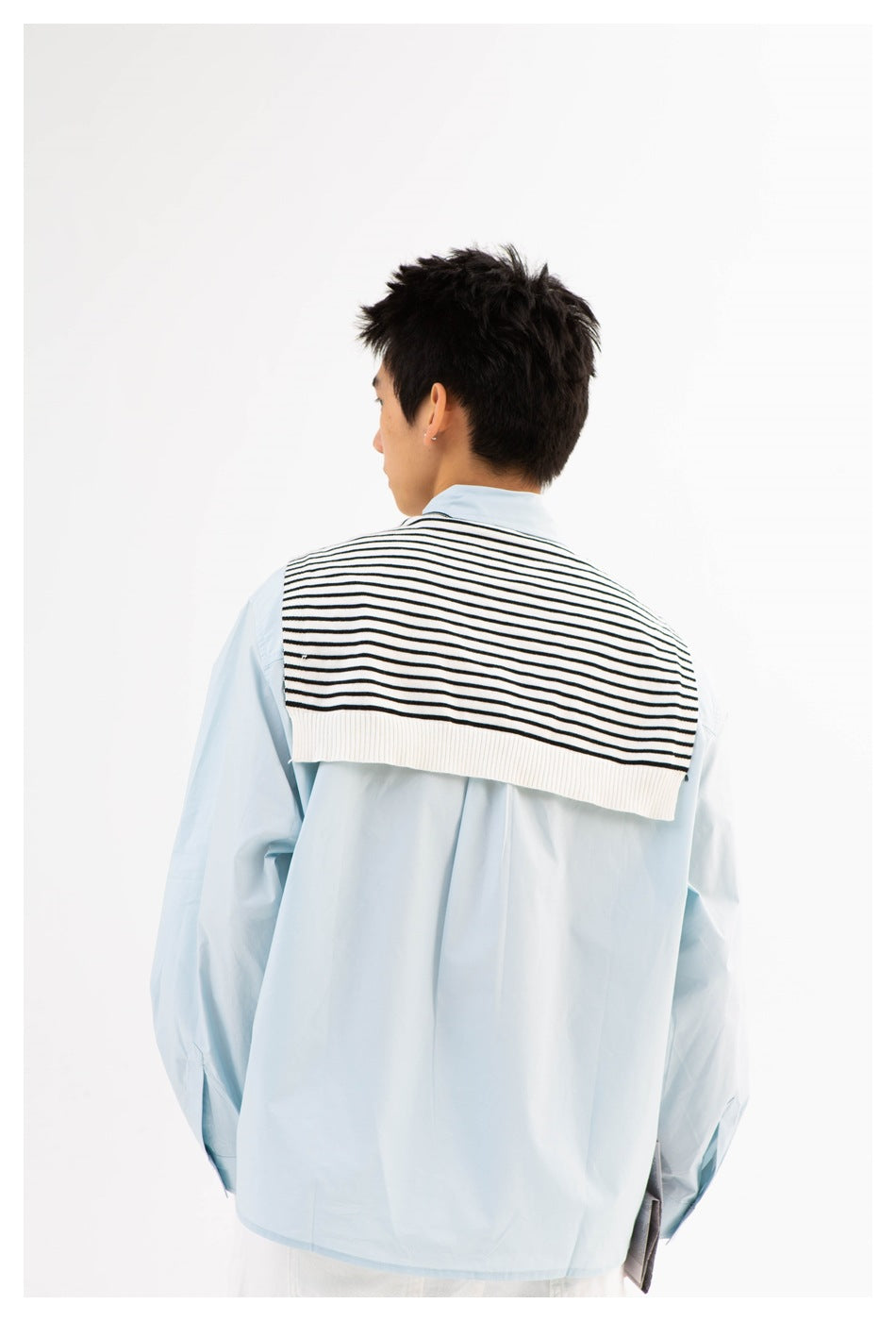 Rear view of a model wearing a pale blue button-up shirt with a black-and-white striped sweater draped across the shoulders.