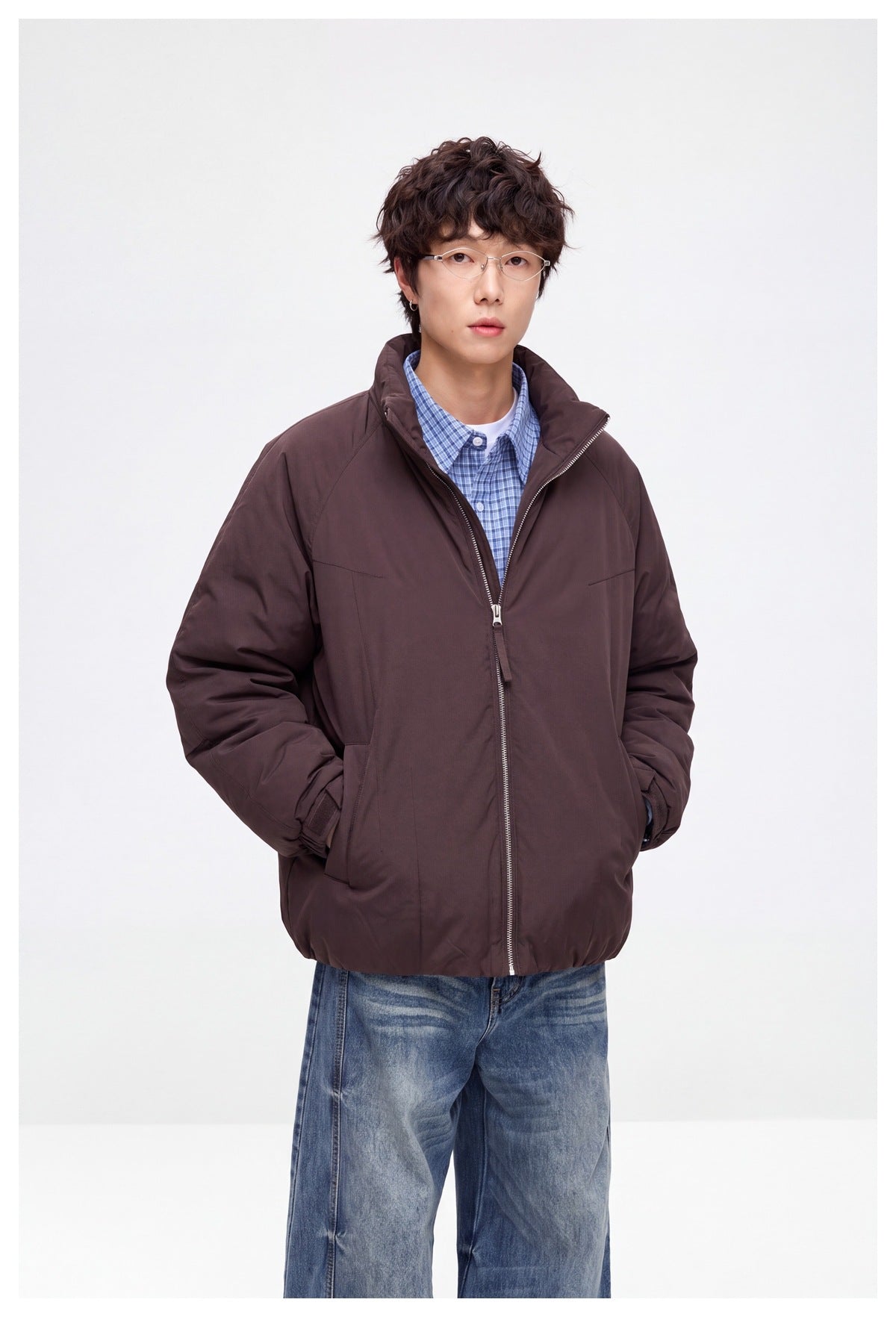 Model wearing a dark brown padded jacket with a raised collar and front zipper over a blue checked shirt.