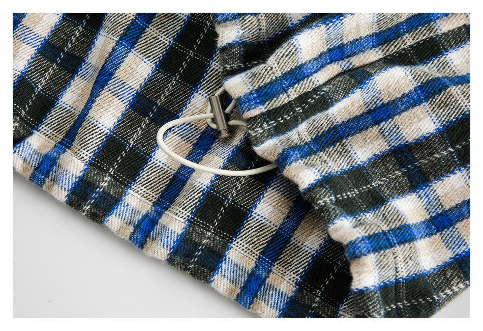 Close-up of a white drawcord and metal toggle on blue, black, and cream plaid fabric.