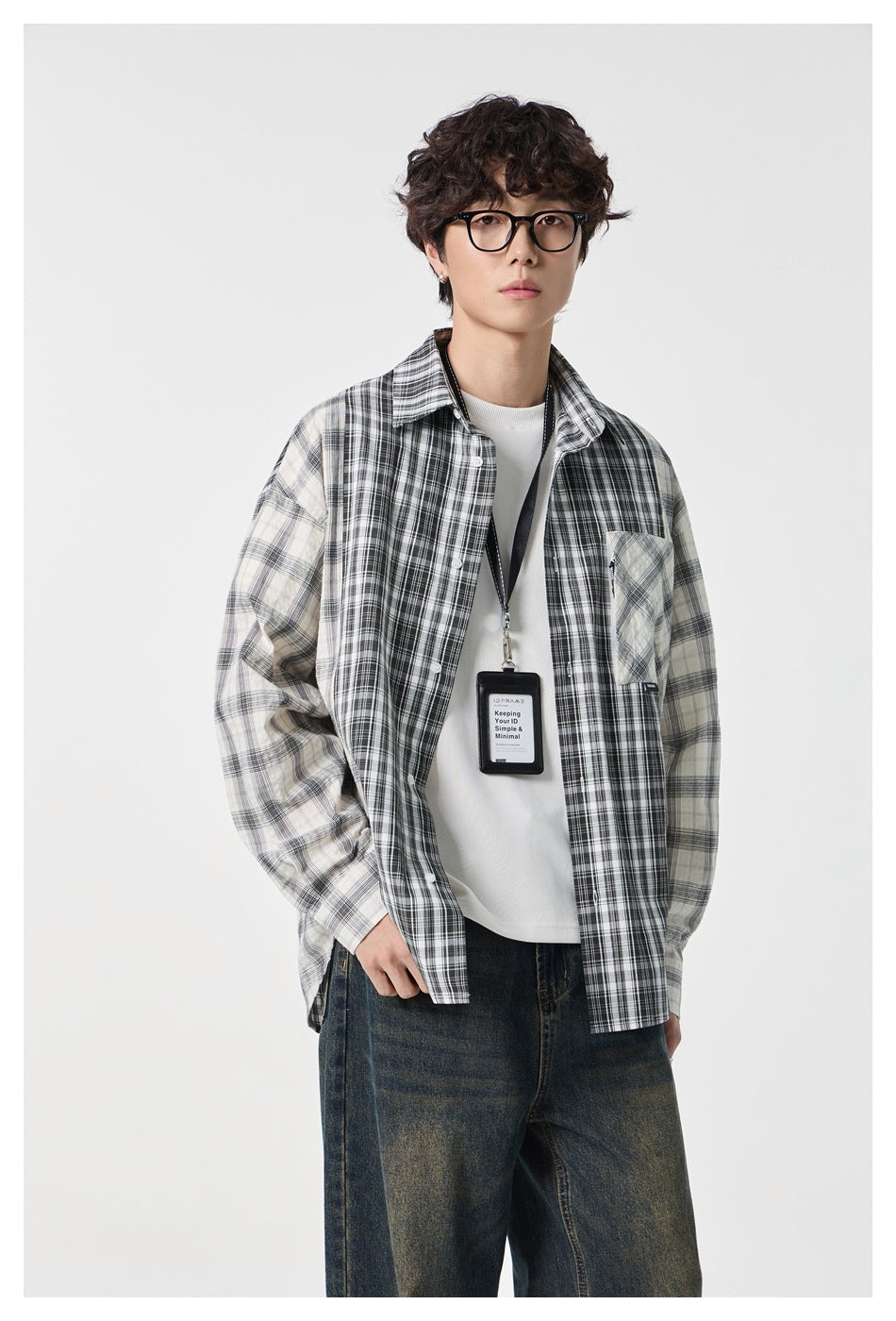 Closer front view of a model wearing an open black and cream mixed-plaid shirt over a white tee.
