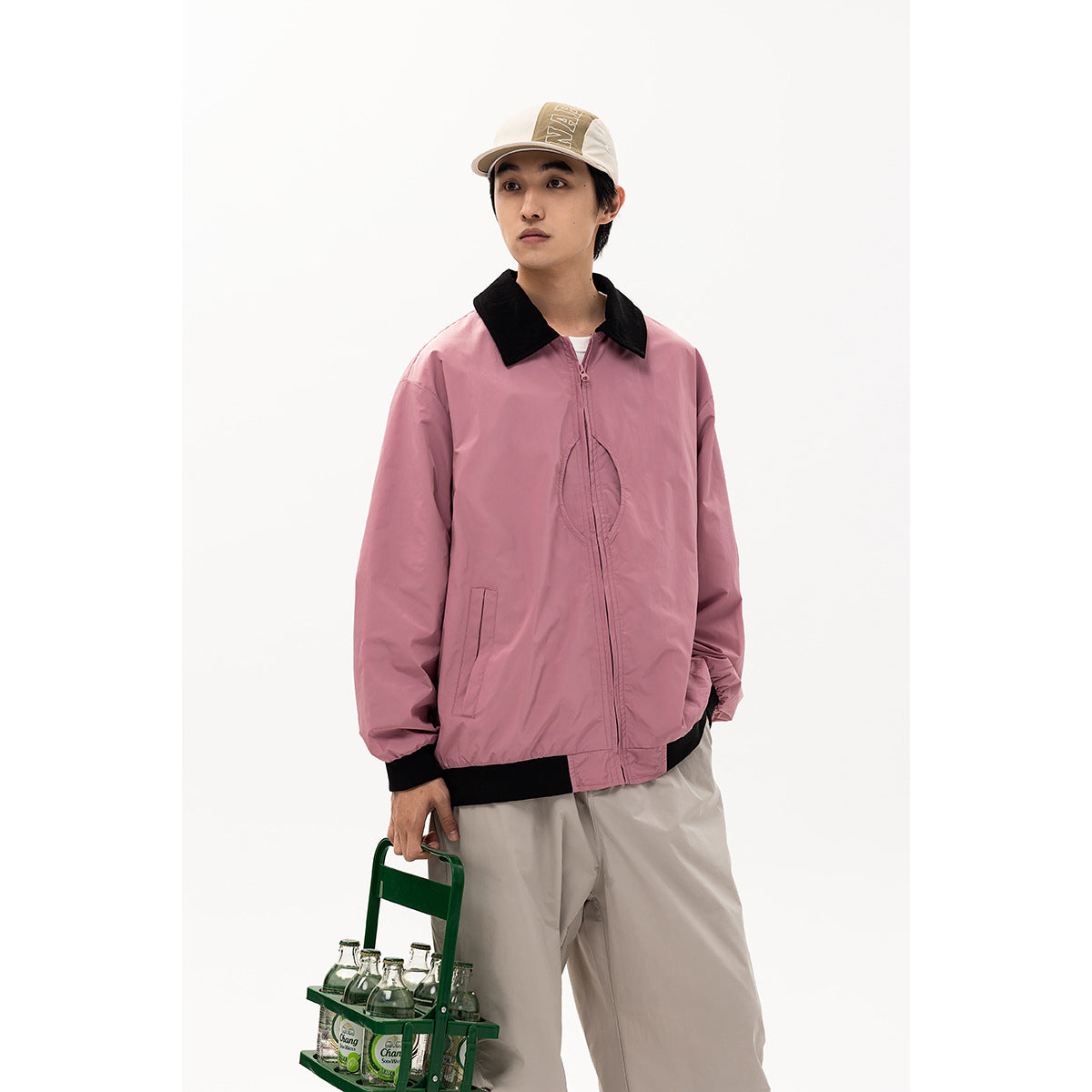 Model wearing a pink jacket with a black collar and trim, beige cap, and light trousers.