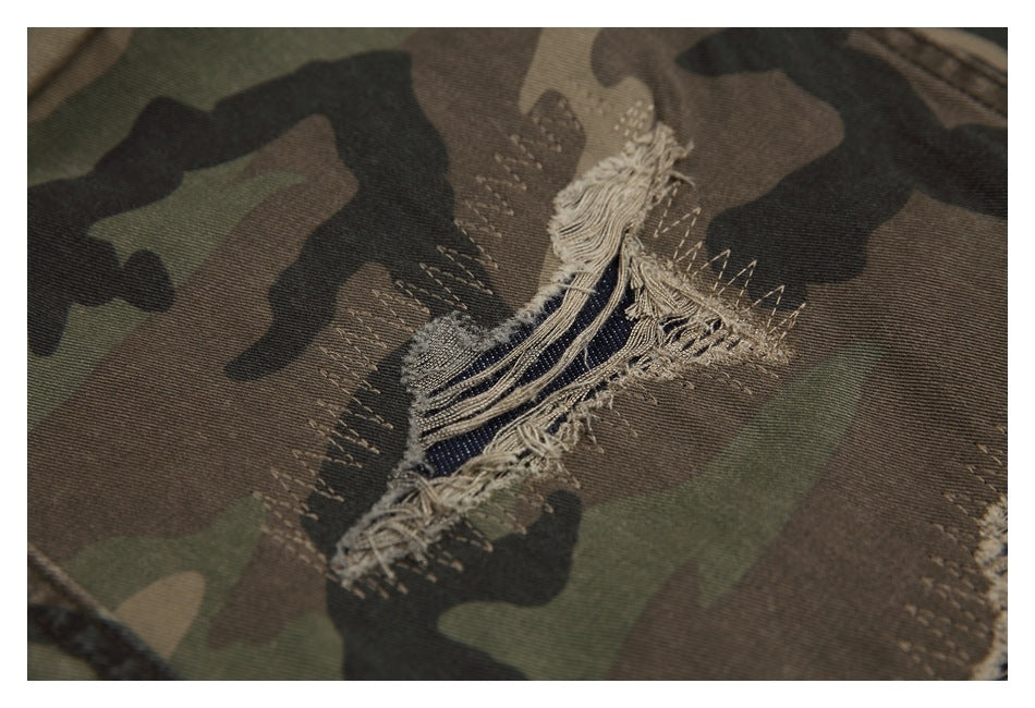 Close-up of a large frayed tear in camouflage pants, exposing dark blue threads.